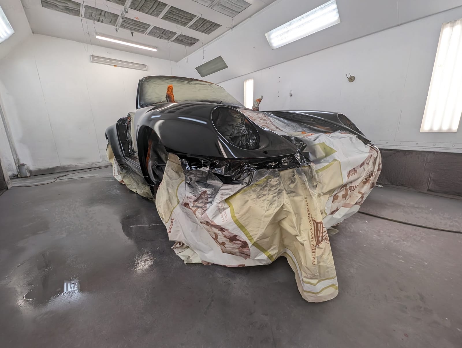 Classic Porsche 911 masked and freshly painted black inside the spray booth